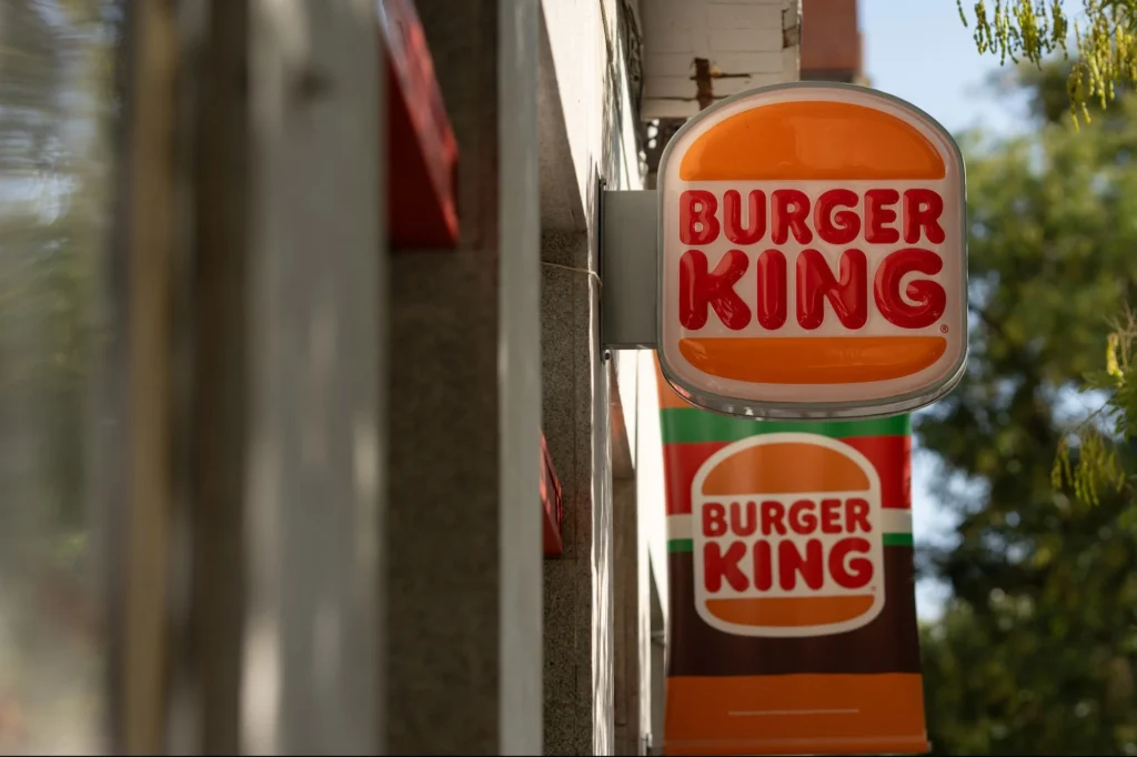 A close-up of a Burger King restaurant sign with the iconic orange and white logo, featuring two stacked burgers. And is best representation of Does Burger King Hire At 14