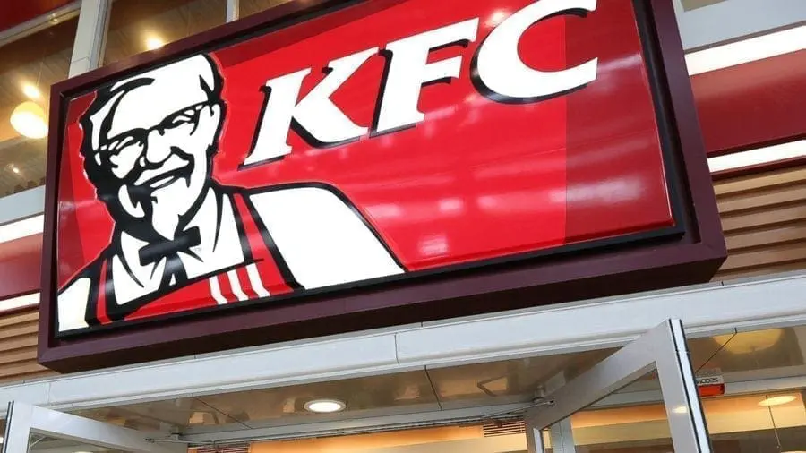 A large KFC restaurant sign with the iconic image of Colonel Sanders smiling. The restaurant is closed and dark inside, with no visible customers or employees. Is KFC open on Thanksgiving?